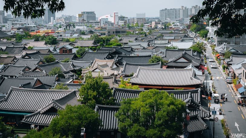 Aerial view of traditional rooftops in Jeonju Hanok Village, South Korea with city skyline in the background.