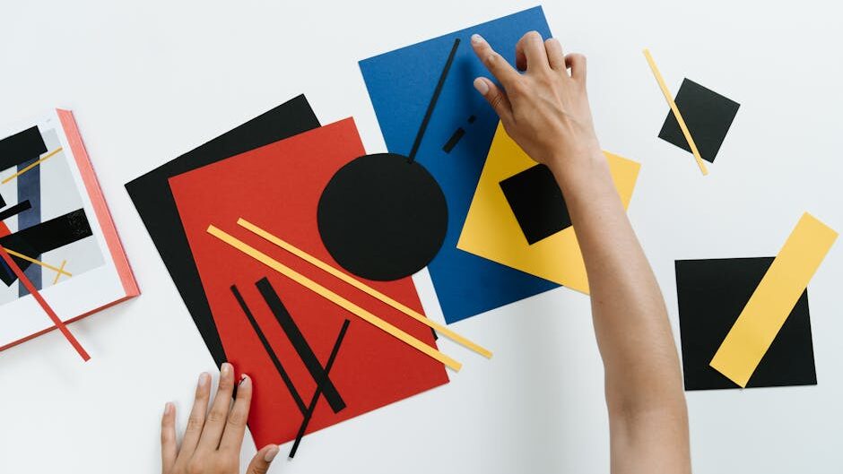 Hands arranging colorful geometric paper shapes in an abstract modern art style.