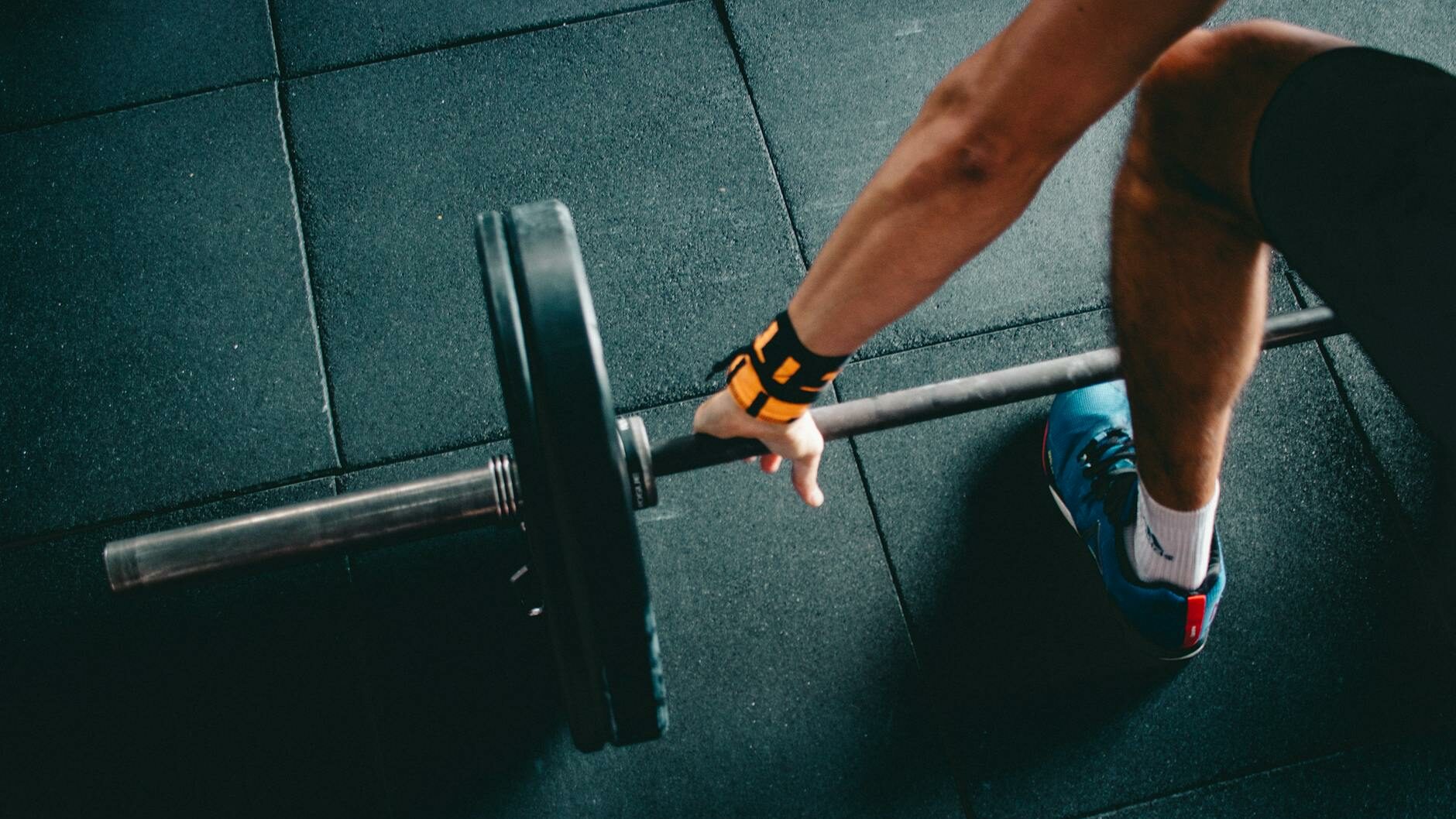 person wearing black shorts and blue lace up low top sneaker holding black barbell